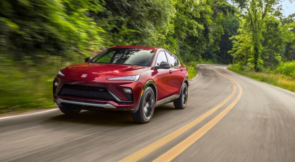A red 2024 Buick Envista ST is shown driving on a tree-lined road after leaving a Buick dealer.