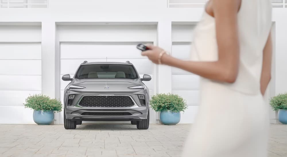 Front view of a woman holding the key fob of a silver 2024 Buick Encore GX parked on a driveway.