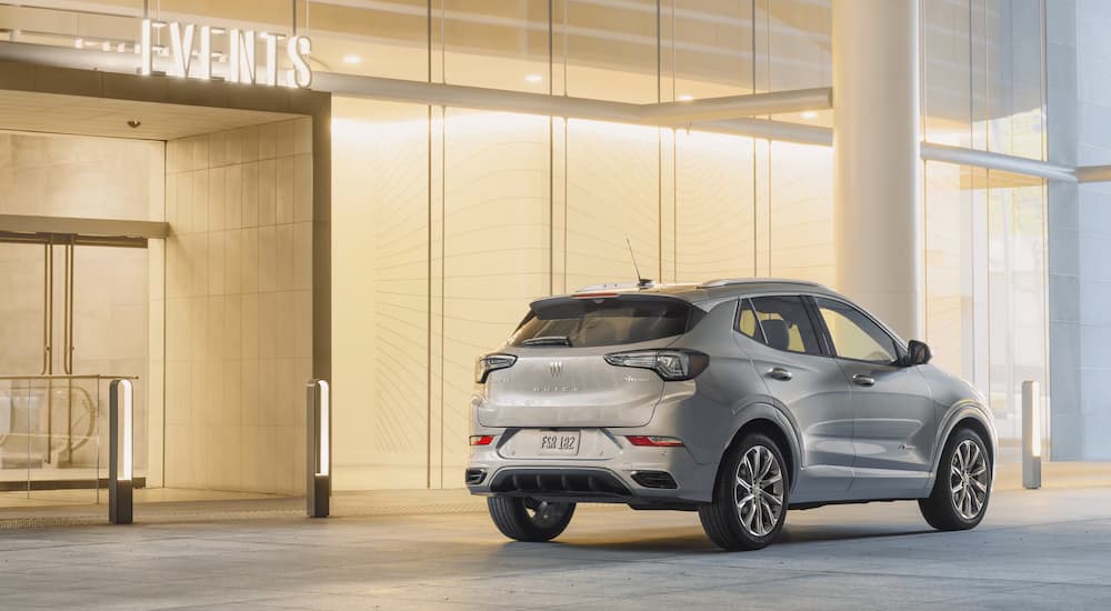 Rear angle view of a silver 2024 Buick Encore GX for sale, parked outside an events building.