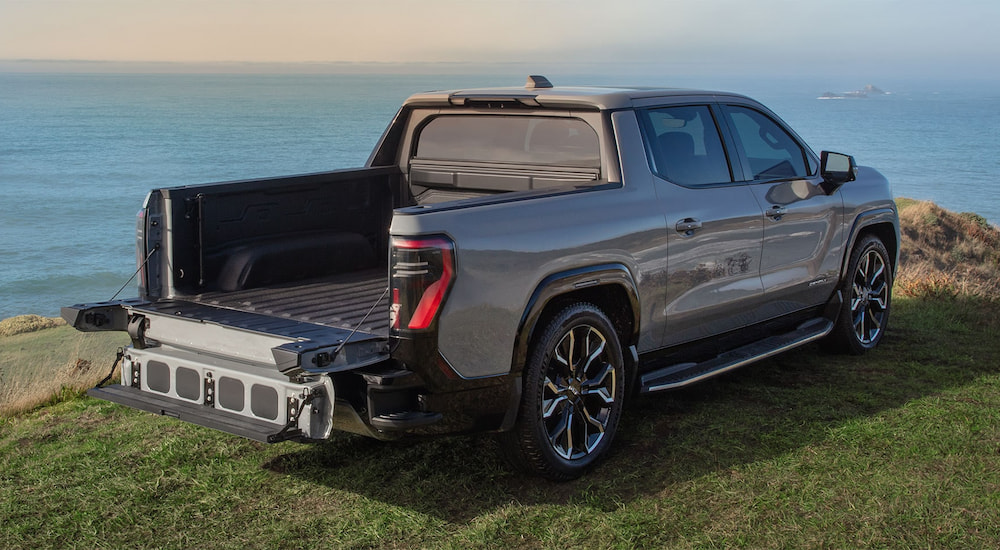 Grey 2026 GMC Sierra EV Elevation with an open tailgate parked on grass.