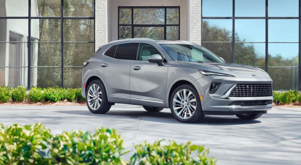 A silver 2024 Buick Envision Avenir shown parked in front of a glass building.