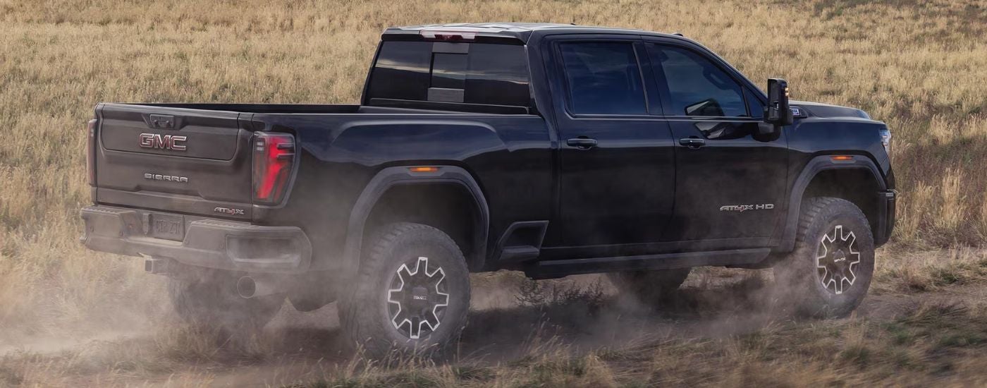 Black 2026 GMC Sierra 2500 AT4X rear view driving on an off-road trail.