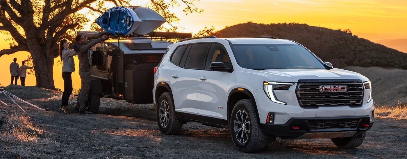 White 2026 GMC Acadia AT4 towing a trailer at sunset