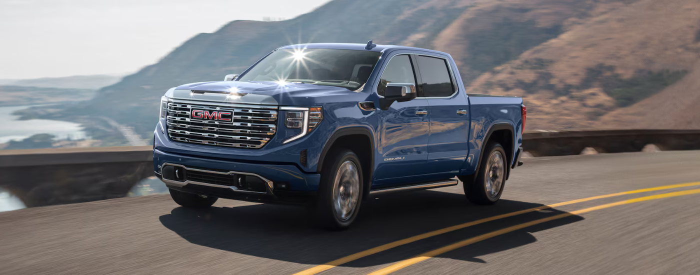 Blue 2026 GMC Sierra 1500 Denali driving along a body of water