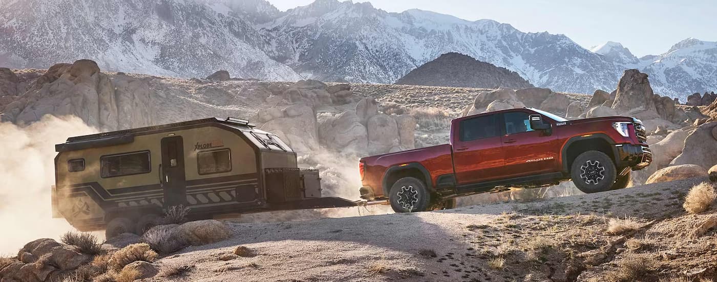 Red 2026 GMC Sierra 2500 HD towing a camper off-road.