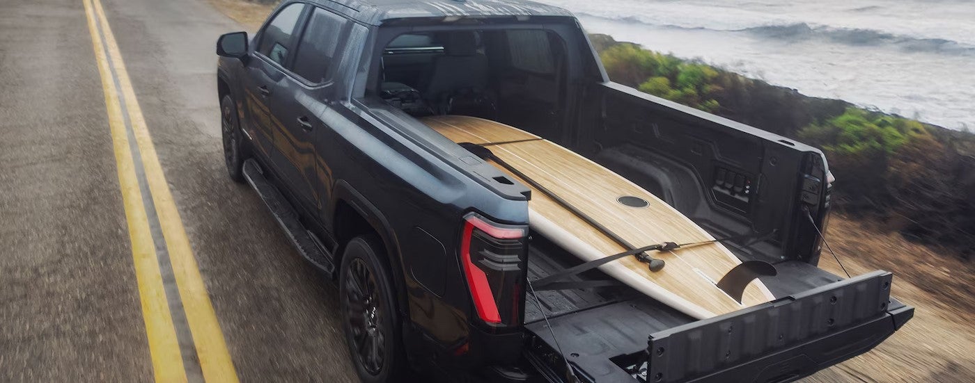 A surfboard strapped down in the bed of a black 2026 GMC Sierra EV Elevation.