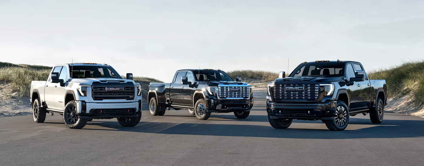 A black 2026 GMC Sierra 1500 Denali, white 2026 GMC Sierra 2500 AT4X HD, and a black 2026 GMC Sierra 3500 Denali parked side by side