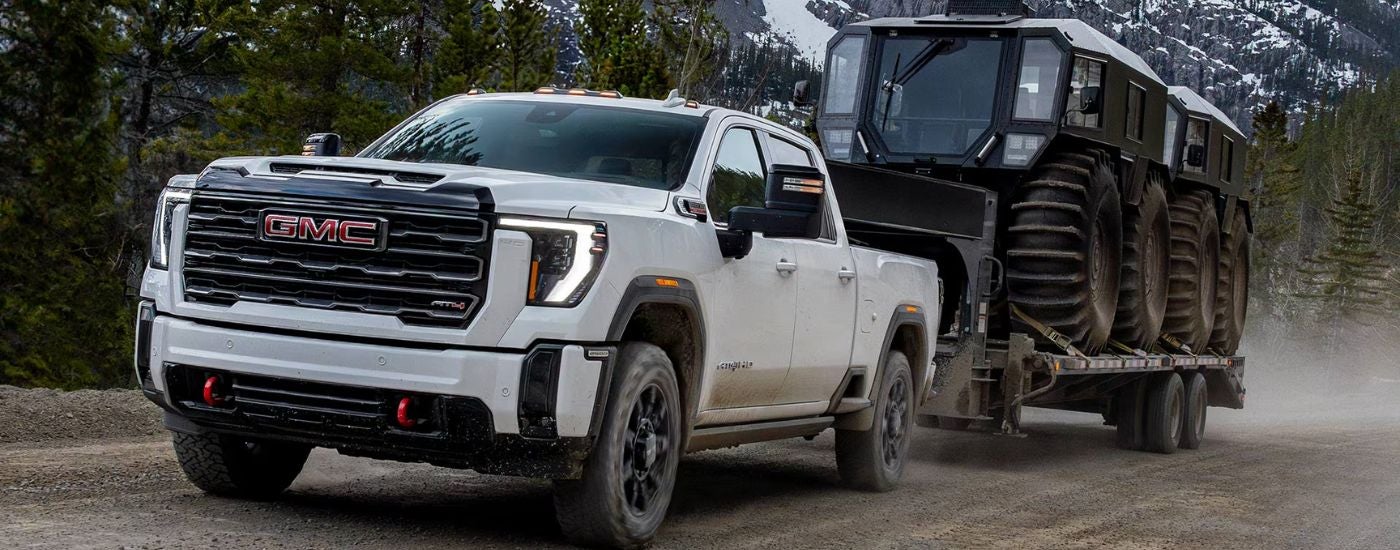 White 2026 GMC Sierra 2500 AT4 towing grooming equipment up a mountain.