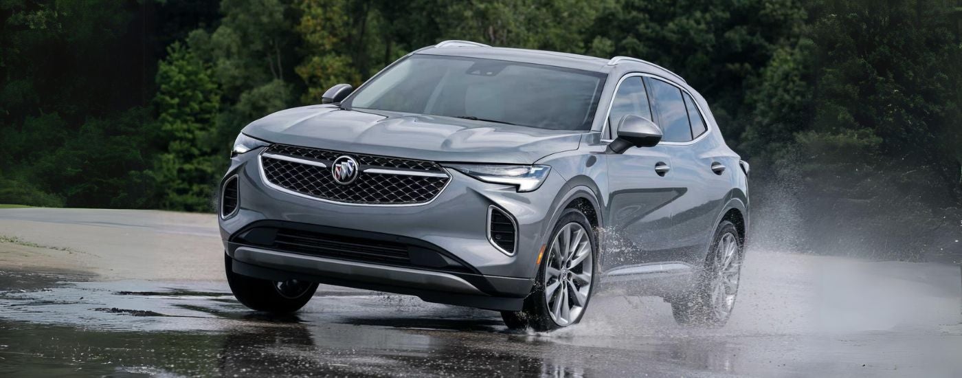 A silver 2023 Buick Envision Avenir shown driving on wet ground.