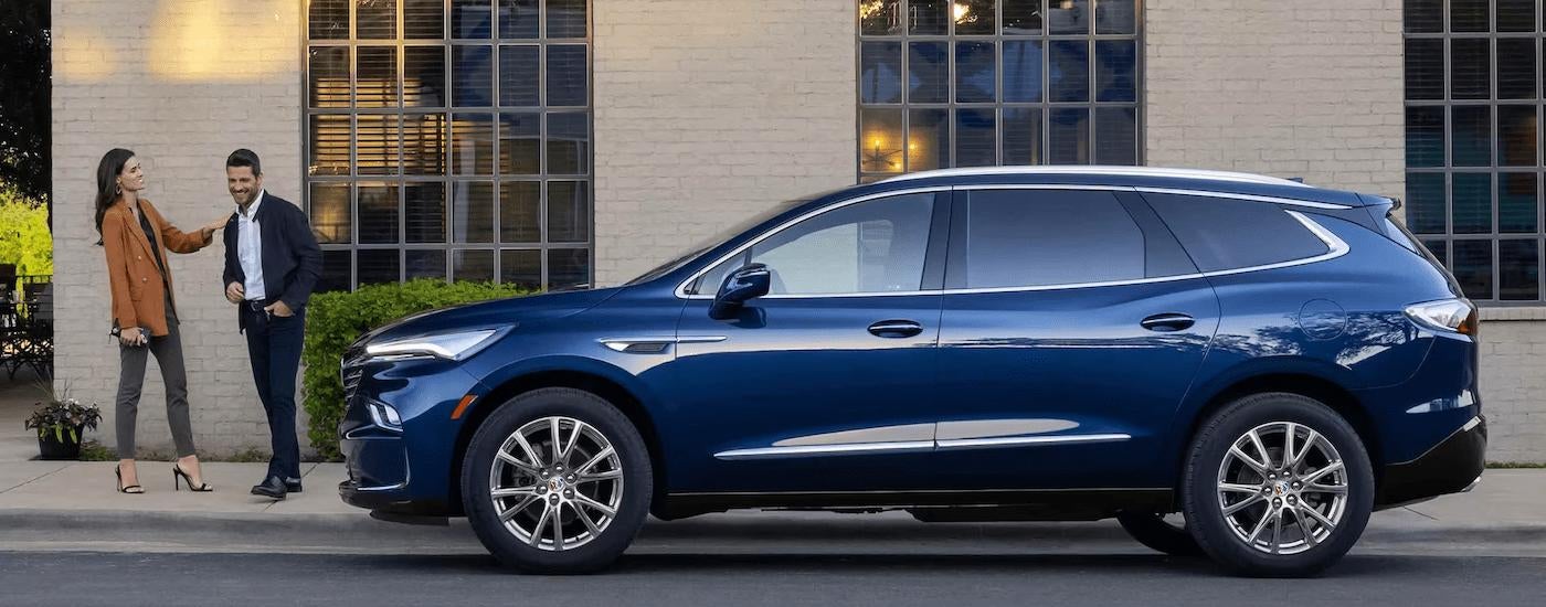 A blue 2023 Buick Enclave is shown parked in near a brick building.