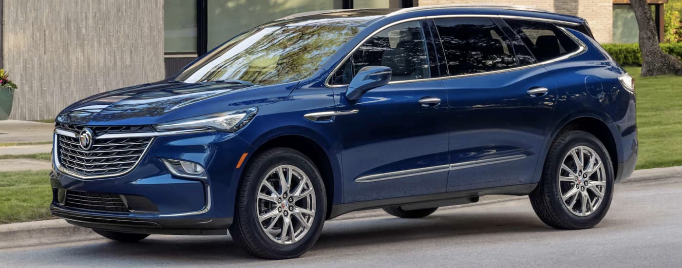 A blue 2023 Buick Enclave is shown parked in near a brick building.
