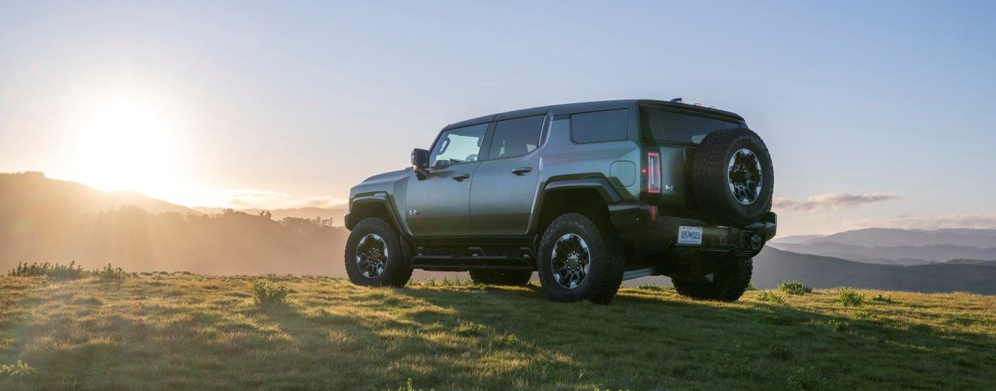 A rear view of a dark green 2024 GMC Hummer EV parked off-road on a trail.