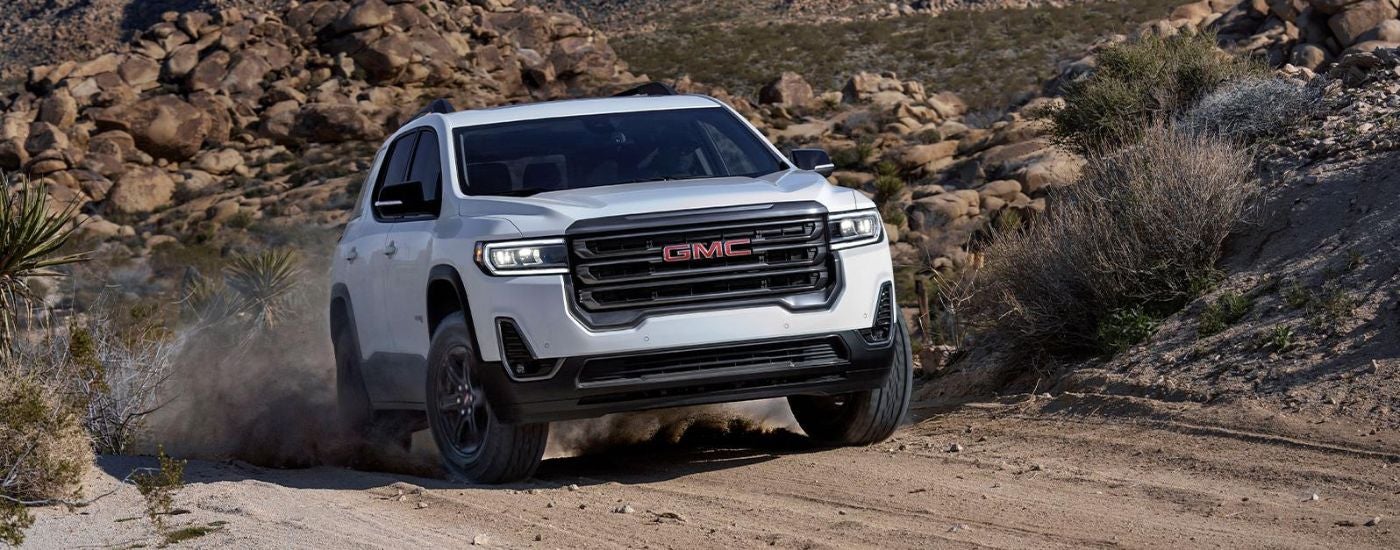 A white 2022 GMC Acadia for sale driving up a desert road.