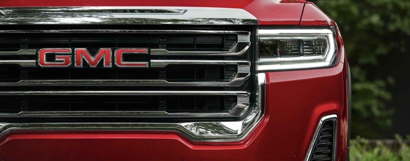 A close-up on the grille and headlight of a red 2023 GMC Acadia SLT.