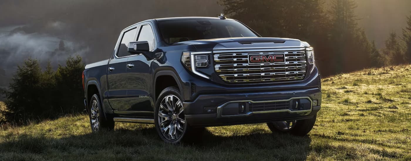A dark blue 2024 GMC Sierra 1500 Denali parked off-road on a grassy hill after visiting a GMC dealer near Brighton.