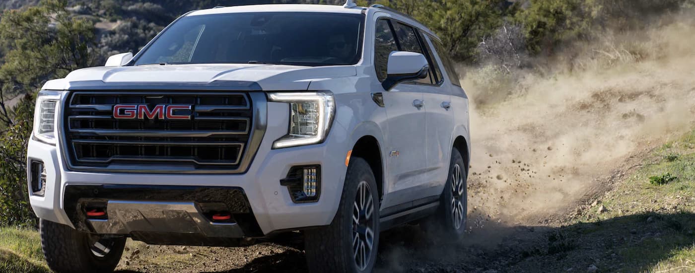 A white 2024 GMC Yukon AT4 driving off-road on a trail.