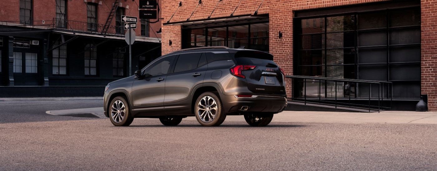 Rear view of a charcoal 2018 GMC Terrain SLT parked in front of brick buildings.