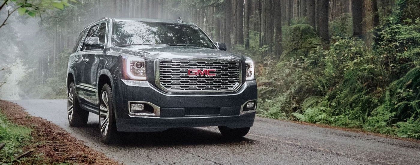 Head-on view of a grey 2020 GMC Yukon Denali driving through the woods to a used GMC dealer.