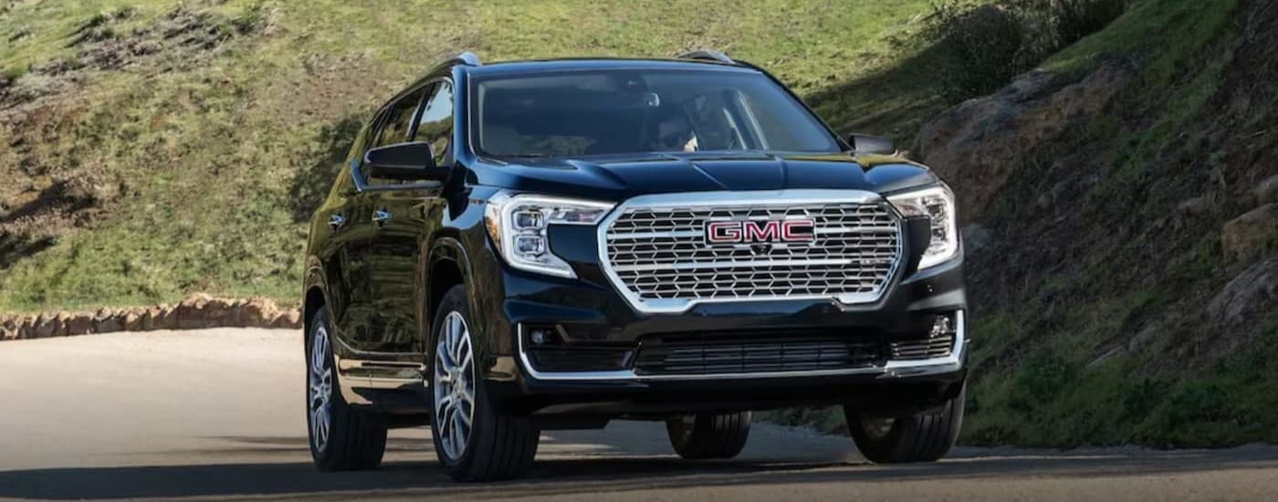 A black 2024 GMC Terrain driving to a used car dealership.